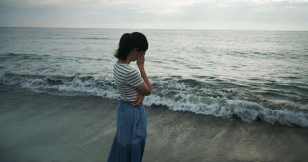 depression and melancholy concept - rear view of asian woman wearing blue skirt is standing at beach and she has negative emotionの写真素材