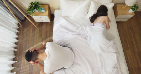 marriage problem relationship difficulties concept - top view of asian young couple sitting separately on bed are sad after having argument and angry conflictの写真素材