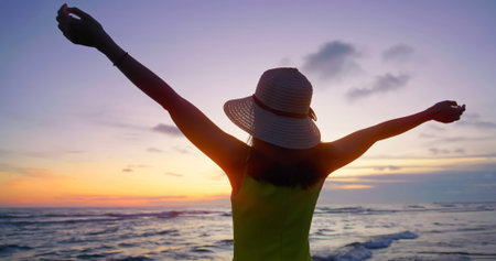 close up of back view young asian woman tourist in yellow dress and hat - she raise hands to sky...