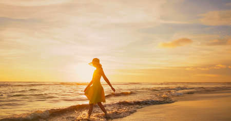 side view of asian woman wearing beautiful yellow dress walking by beach at golden sunset - Female tourist on summer vacationの写真素材