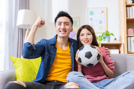 a happy couple watching soccer game on a laptop at home discussing about the competition - man poses fistの写真素材