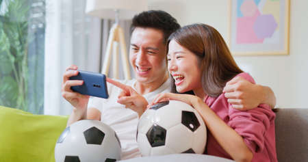 asian happy couple watching soccer games on the smartphone together at home with full of excitement and happinessの写真素材