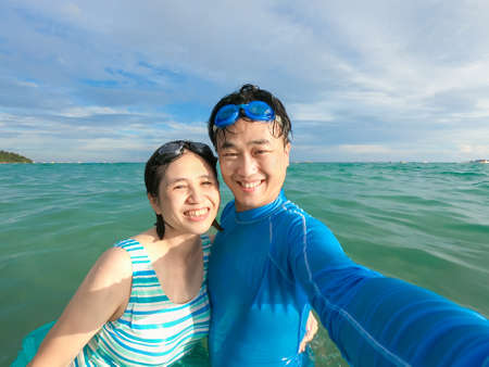 point of view asian married couple wear swimsuit use phone take selfie together on sea - they do water activities while summer vacation in Kentingの写真素材