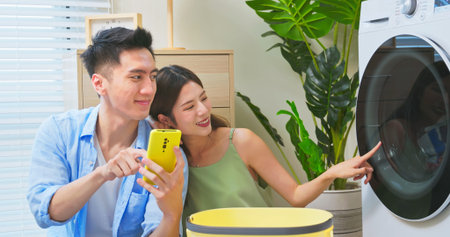 asian couple is using phone to control the washing machine when cleaning clothes