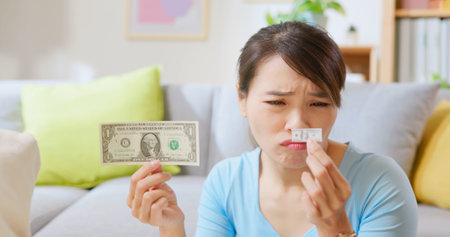 worried asian woman holds US dollar comparing two size paper money at home - economic inflation...