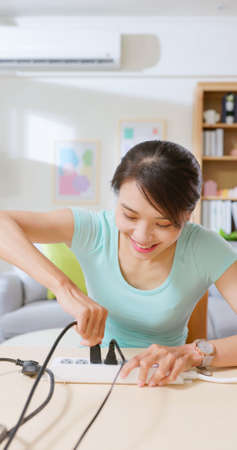 vertical of happy asian woman smiling pull out or in plugs from socket for eco friendly and electricity bill savingの写真素材