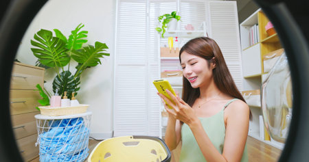 point of view asian woman doing laundry with smartphone controllingの写真素材