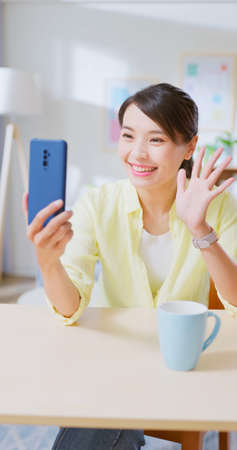 Asian woman sitting on chair using smartphone has video call with friends or family feeling happy smiling when relax in living room at homeの写真素材