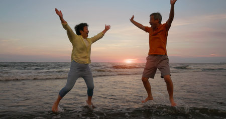 close up of asian elderly carefree couple standing on the beach and smiling at you happily in sunset...