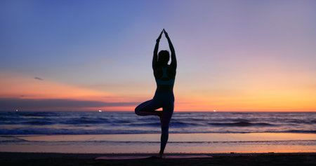 silhouette of Asian healthy woman is practicing yoga and meditation on beach in the duskの写真素材