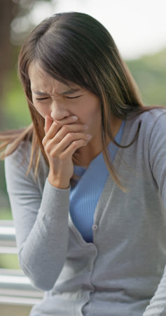 close up of sick asian woman sitting on bench is coughing and has sore throat in parkの写真素材
