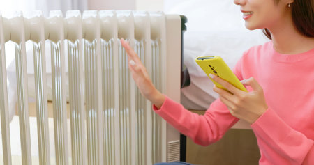 side view of asian woman covering blanket wearing wool hosiery feel cold using radiator heater to...