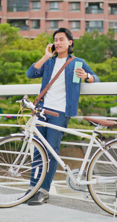 asian man talking on phone holding bottle in the city to commute with his bike besideの写真素材