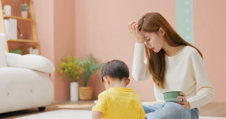 asian worried mother is feeding kid with spoon but unbehaved child eat lessの写真素材