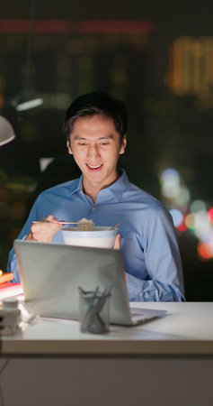 Asian business man eating instant noodle and watching drama in office at night