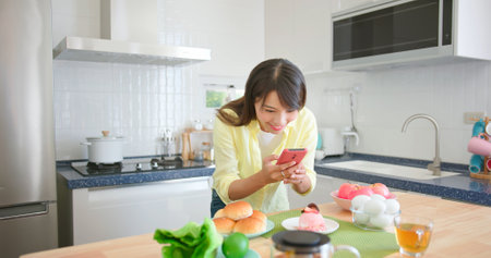 asian female photographer is using smart phone to take pictures in kitchen and she satisfied with the workの写真素材