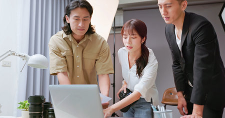 Female Asian photographer reviewing products using computer with crews or clientの写真素材