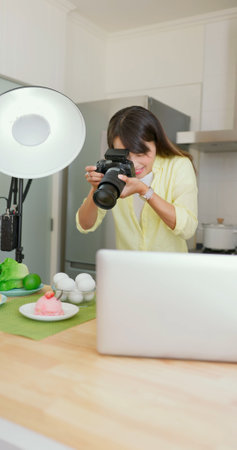 asian female photographer is using digital camera to take pictures in kitchenの写真素材
