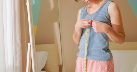 asian unhappy woman is dissatisfied while she measuring her chest and breast in front of mirrorの写真素材