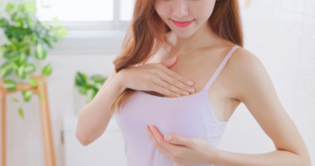 breast cancer self check concept - asian woman is touching her chest to prevent sick at homeの写真素材