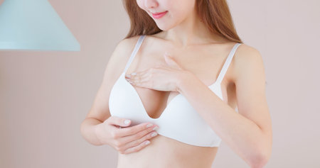 breast cancer self check concept - asian woman is touching her chest to prevent sick at homeの写真素材