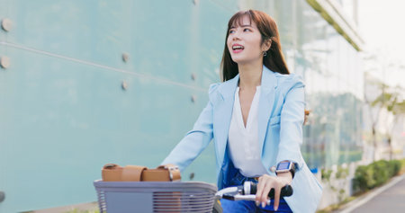asian happy woman is riding a sharing bike commuting to work in the cityの写真素材