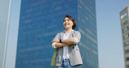asian confident businessfemale standing outdoor has crossed arm in city and looking far awayの写真素材