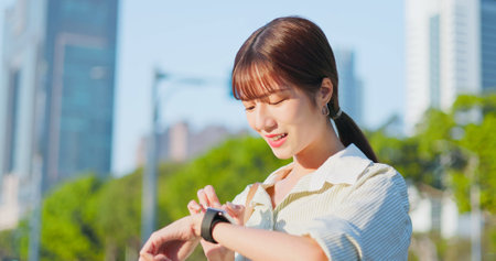 asian happy woman is leaning by railing at platform and waiting for tram or train - using smart watchの写真素材