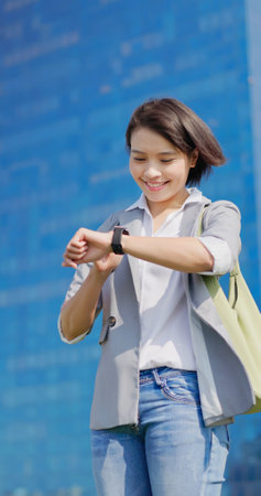 asian smiling businessfemale standing outdoor is looking on her smart watch in cityの写真素材