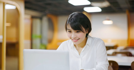 asian cheerful businesswoman is sitting on chair and working with laptop computer in officeの写真素材