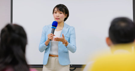 asian female teacher is speaking in adult education class - students sitting on chair listening the lectureの写真素材