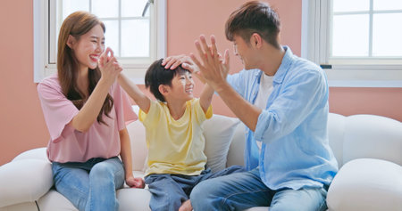asian parent happy with kid growing up - father mother son sitting on the sofa with high five gesture so much fun such a good family interaction relationshipの写真素材