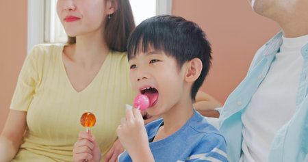closeup asian children eat unhealthy high calories sugary food sweet candy lollipops watching TV with father and mother - parenthood ignorant carelessの写真素材