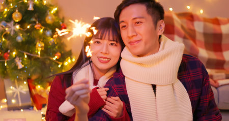 asian lovely young couple are playing sparklers fireworks happily with decorated christmas tree on xmas at homeの写真素材