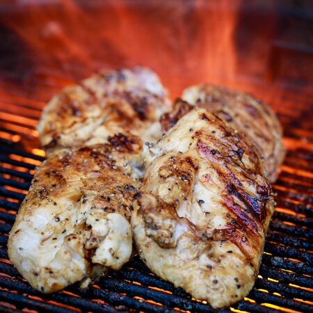 Four chicken breasts on charcoal grill with flame in the backgroundの写真素材