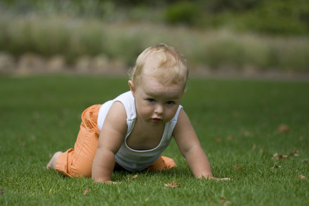 Adorable baby with white vest crawling on grass, looking straight aheadの写真素材