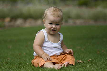 happy baby, sitting on grass wearing white vest and orange shorts.の写真素材