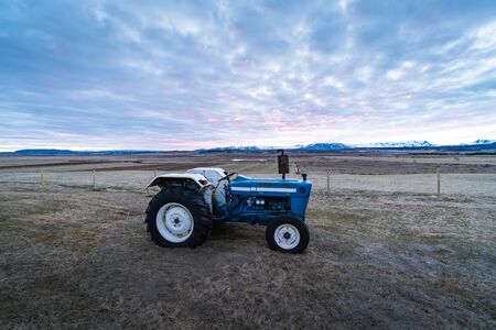 Agriculture stock picture. A small tractor on a field during the sunset time. Agriculture in Iceland, Scandinavia. Background photograph of a tractor.の写真素材
