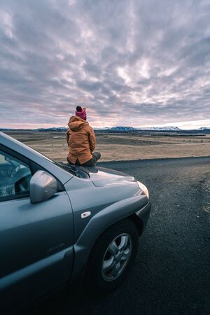 Road trip is calling. Time for the road adventure begins. A young solo female adventure traveler in a nature with beautiful sunset sky. Iceland travelの写真素材