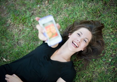 A young happy girl lying on the grass laughing at her phoneの写真素材