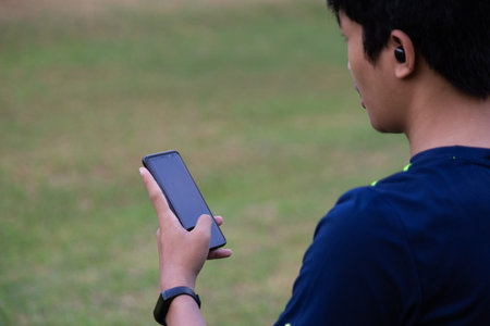 young fitness man at the park wearing wireless earphones and smart watch checking mobile phone