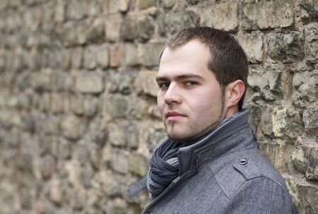 Young Man In Gray Coat Posing Near Old Wallの写真素材