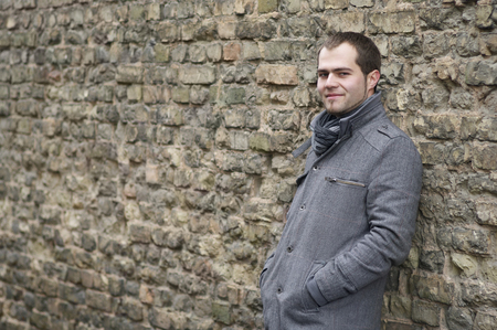 Young Man In Gray Coat Smiling Near Old Brick Wallの写真素材