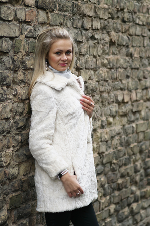 Upset Young Woman In White Fur Coat Near Old Brick Wallの写真素材