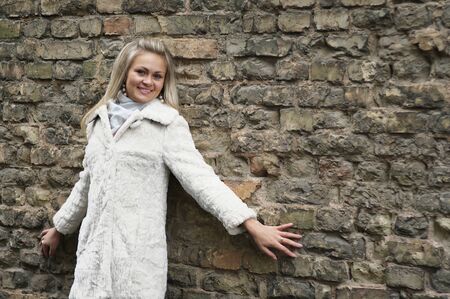 Young Happy Woman In White Fur Coat Near Old Brick Wallの写真素材