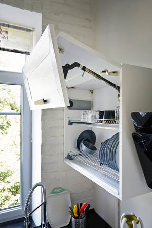 Completely Opened White Kitchen Cabinet with Plates and Glasses on Shelfの写真素材