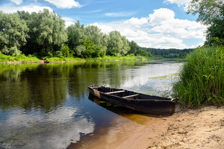 Old rotten rowing boat on green summer beach under blue sky with white clouds at noon Neman River Grodno Belarusの写真素材