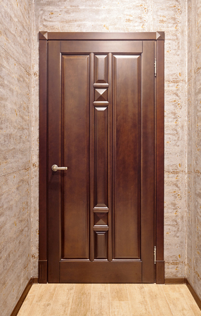 Brown metal with wooden overlays entrance door with brass handle in corridor with floor tiled in beige tonesの写真素材