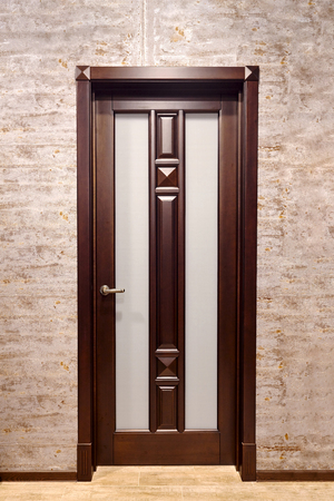 Brown metal with wooden overlays entrance door with brass handle and frosted matte glass with floor tiled in beige tonesの写真素材