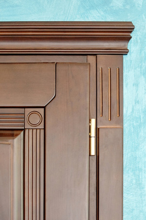 Element of wooden door in frame of brown wood carved geometric ornaments classical style with gilded hinges on blue plastered wall background close upの写真素材